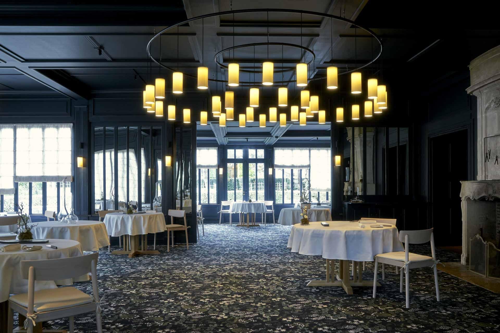 Restaurant gastronomique de haute cuisine à l’Hôtel Les Sources de Caudalie, avec des tables rondes et un élégant chandelier suspendu. L’espace est parfait pour les dîners de luxe.