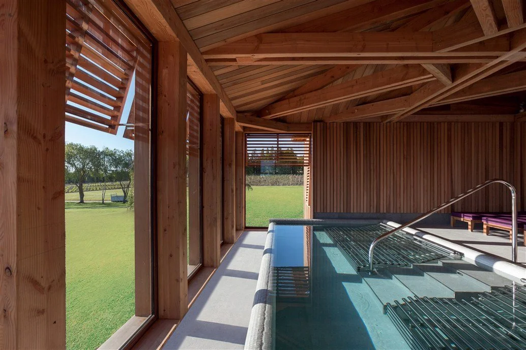 Piscine intérieure chauffée de l’Hôtel Les Sources de Caudalie, dans un espace moderne en bois avec de grandes fenêtres donnant sur le vignoble. Il est idéal pour se détendre avec des vues naturelles.