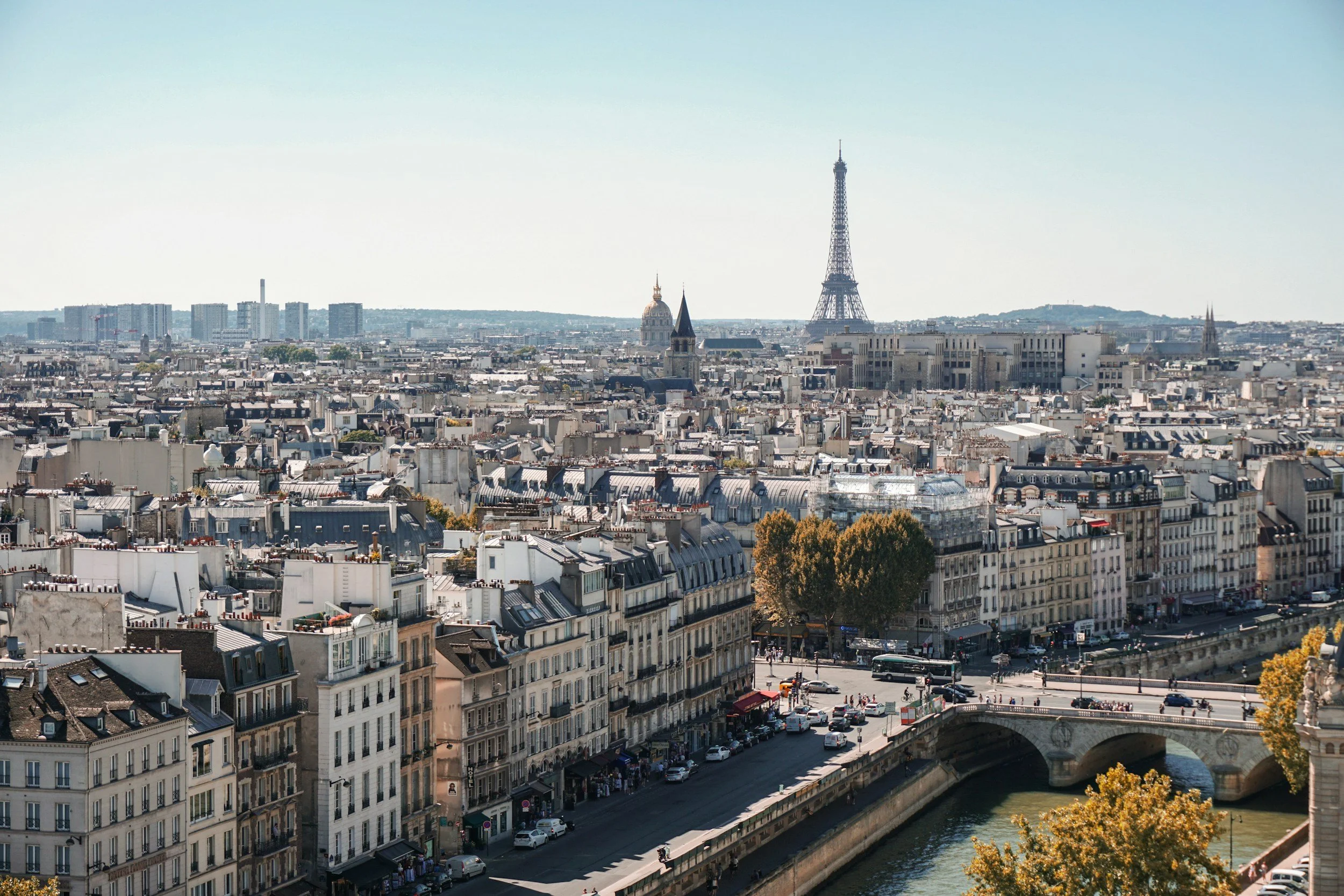 Vue panoramique de Paris avec la Tour Eiffel en arrière-plan, des bâtiments résidentiels en premier plan, une rivière et un pont.