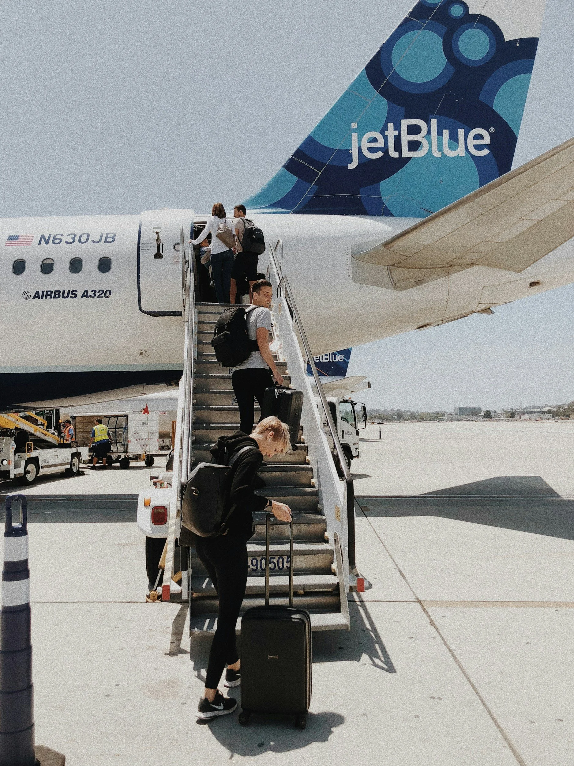 Personnes faisant la queue pour embarquer dans un avion JetBlue sur le tarmac de l'aéroport, avec des valises et des bagages à main.
