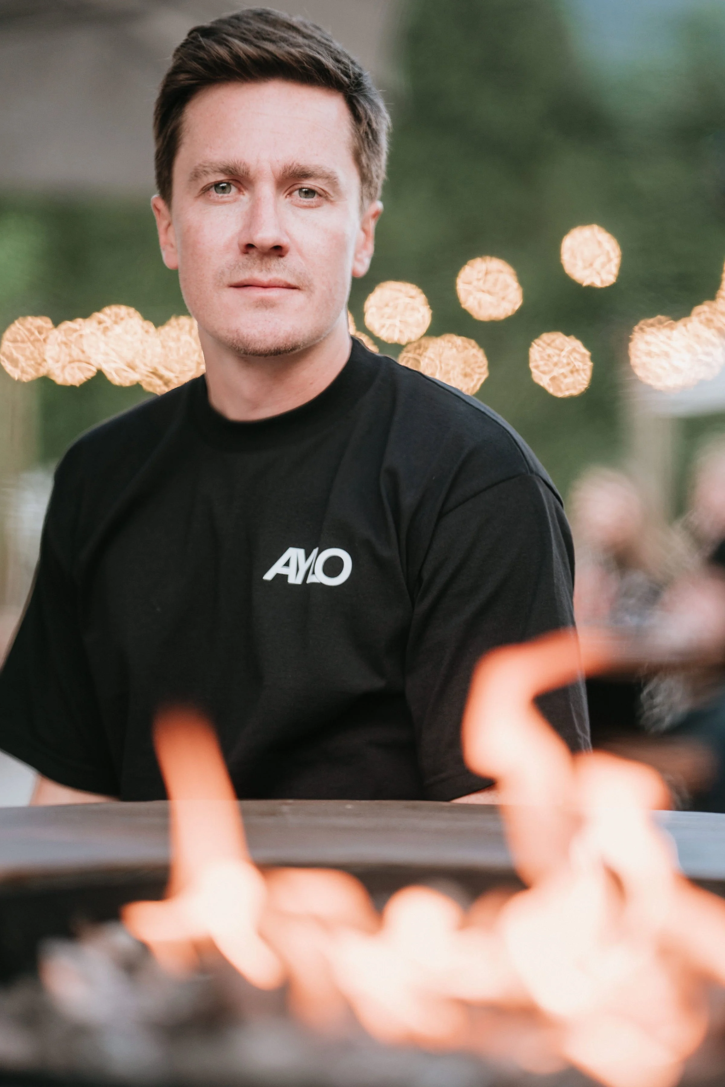 Jeune homme avec t-shirt noir assis à une table, flou d'une passion de feu au premier plan.