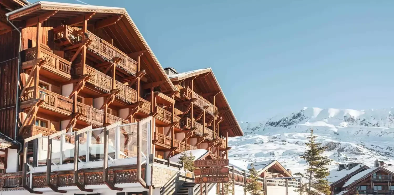Façade avec spa : Vue de la façade du Hôtel Chamois d’Or 5* à L’Alpe d’Huez, montrant l'architecture de bois du chalet et un espace spa extérieur avec jacuzzi.