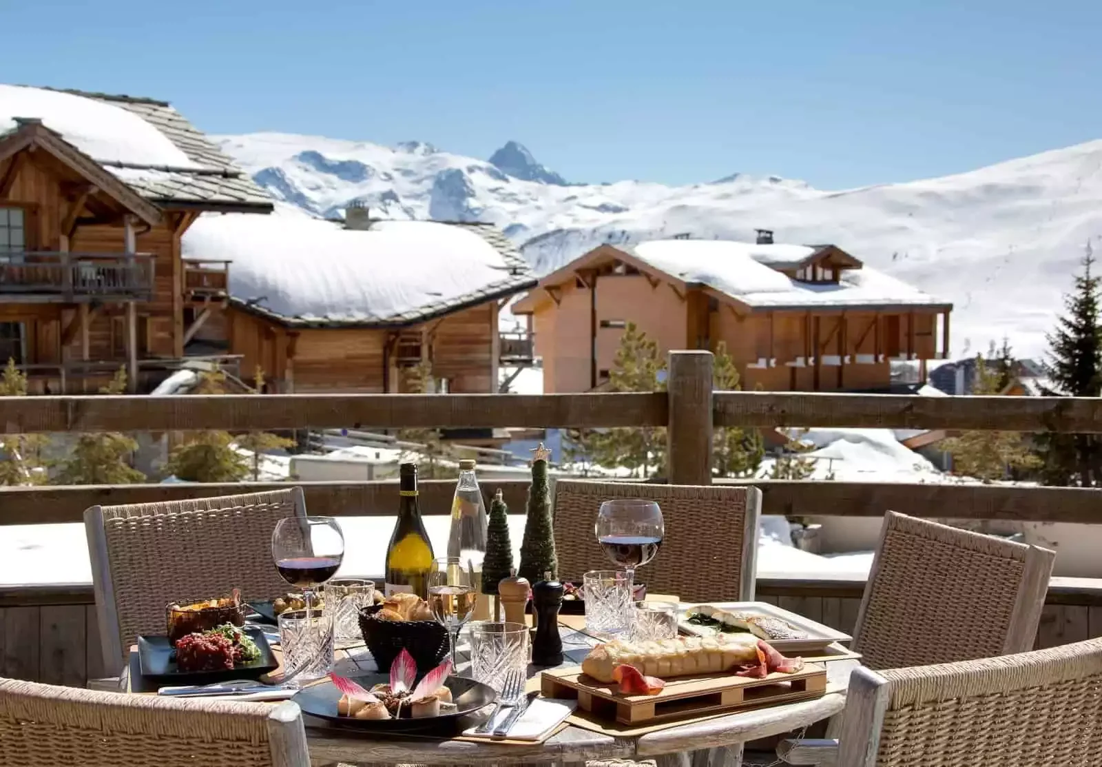 Terrasse extérieure de restaurant à l'Hôtel Chamois d'Or 5* à L'Alpe d'Huez, avec une table dressée pour un repas et une vue imprenable sur les chalets et montagnes enneigées. Idéal pour un séminaire Aylo Montagne.