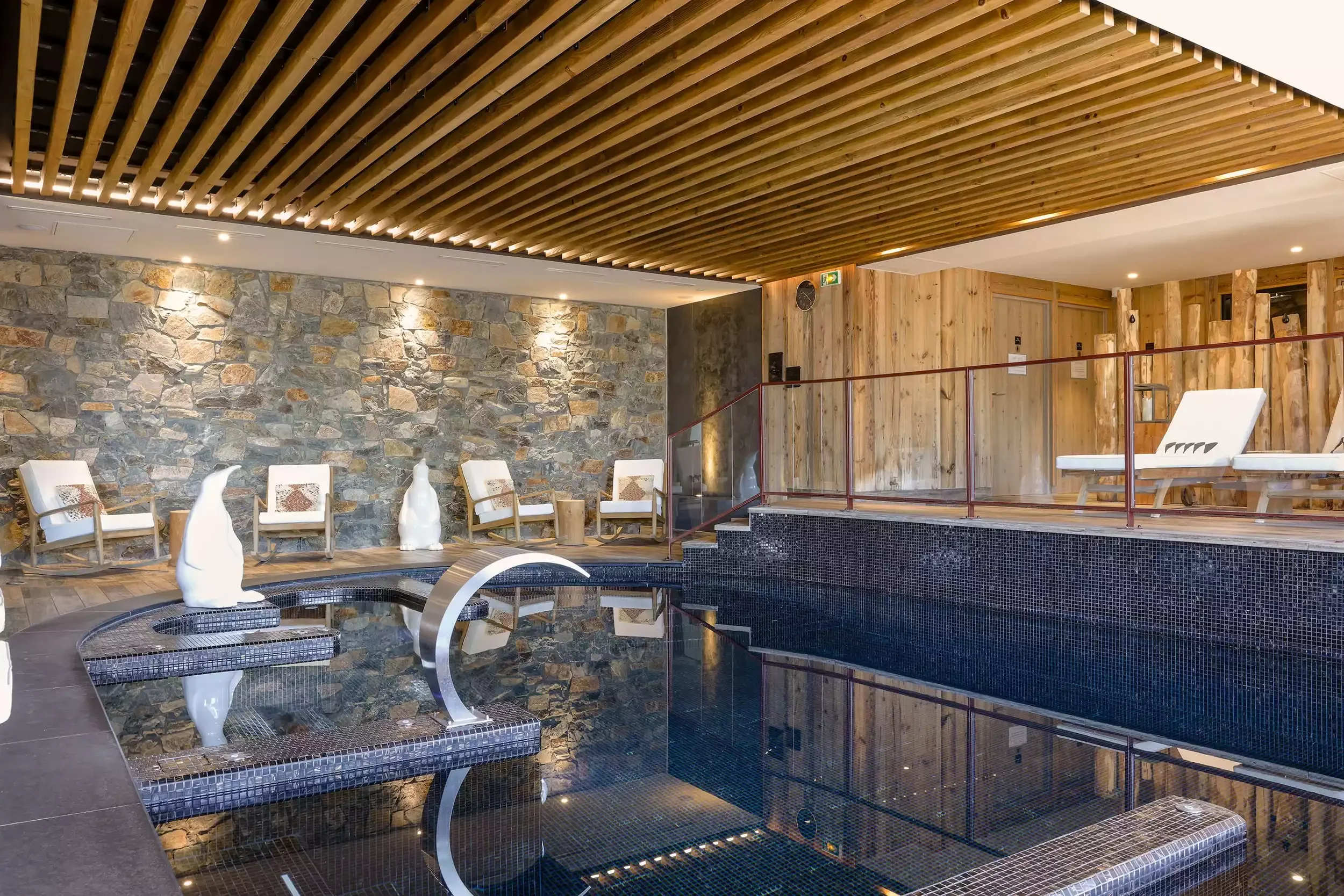Piscine intérieure du spa de l'Hôtel Grandes Rousses 5* à L'Alpe d'Huez, avec des murs en pierre et boiseries. Un espace de sérénité et bien-être pour les pauses d'un séminaire Aylo Montagne.