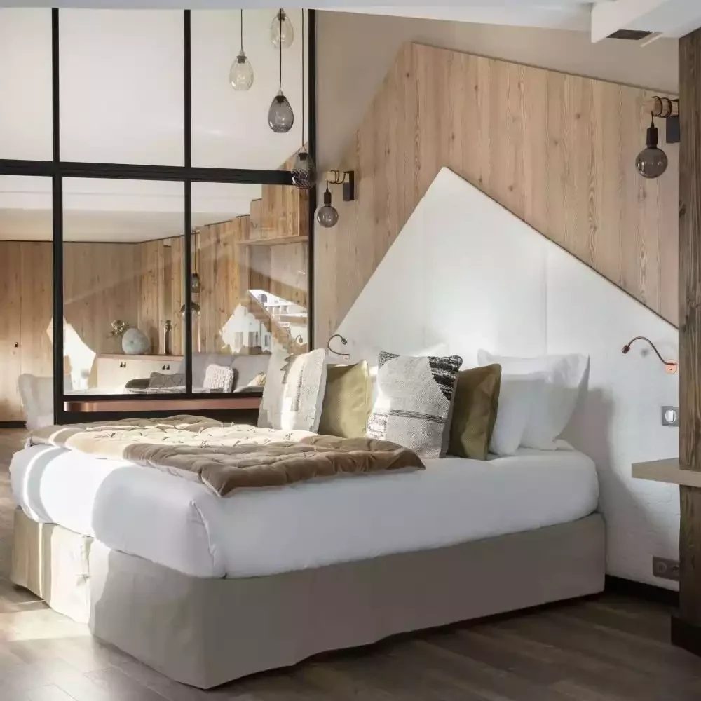 Chambre de luxe à l'Hôtel Grandes Rousses 5* à L'Alpe d'Huez, avec design moderne mêlant bois clair, tête de lit capitonnée et textiles élégants. Confort optimal pour un séminaire Aylo Montagne