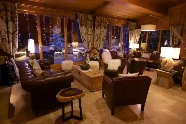 Salon ou bar du **Hôtel Neige et Roc ****, avec des fauteuils en cuir, des tables en bois et un éclairage chaleureux, créant une atmosphère accueillante pour se détendre.