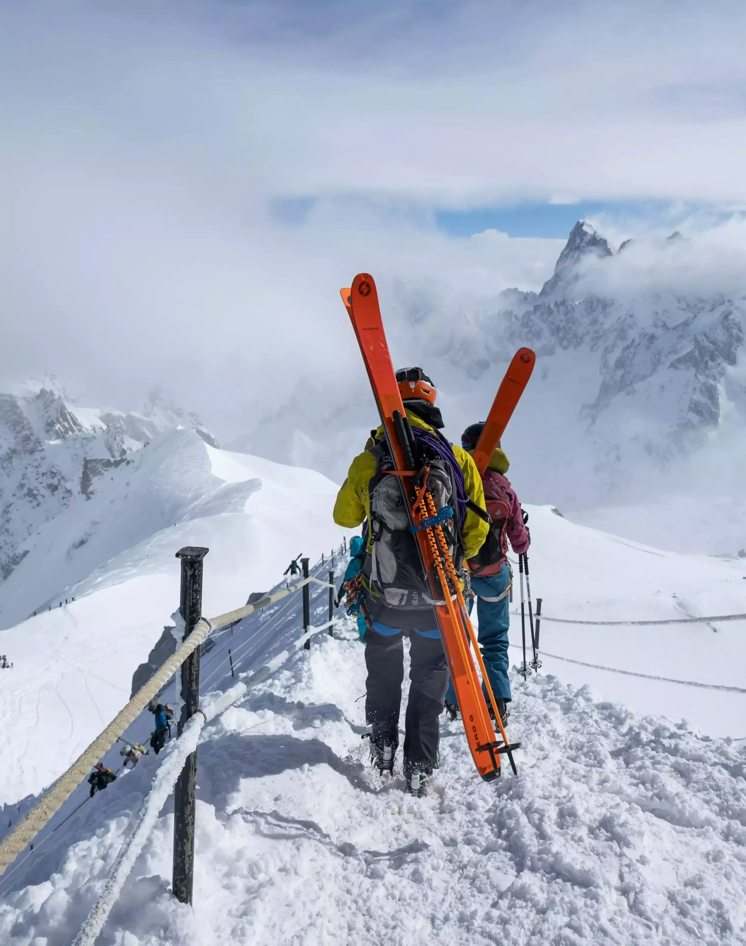 deux participants à un séminaire d’Aylo Montagne à Chamonix, faire du ski de randonnée et marcher avec leurs skis sur une crête de montagne enneigée.
