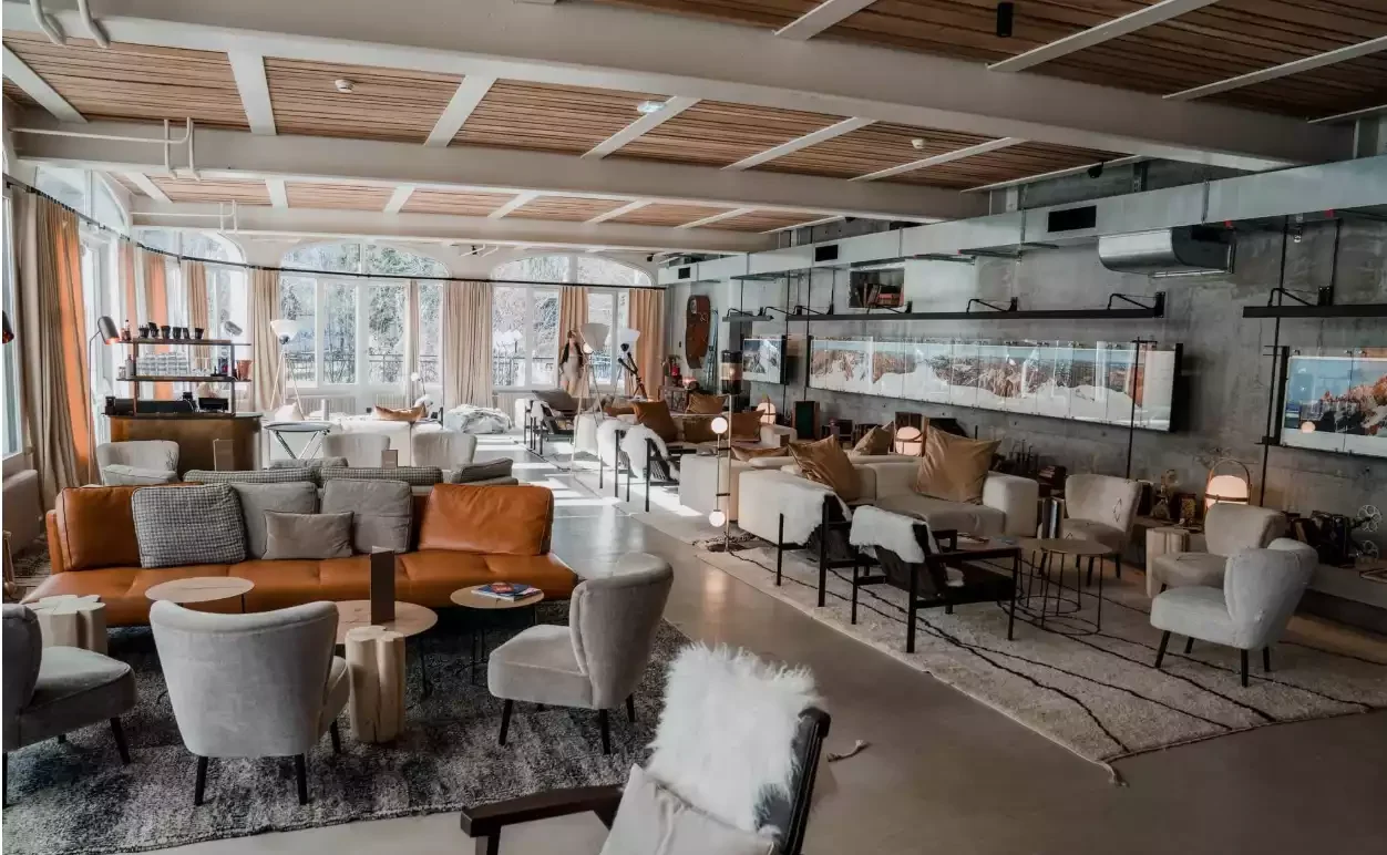 Grand salon ou lobby à l’Hôtel La Folie Douce 4*, avec canapés en cuir et fauteuils modernes, créant une ambiance cosy et sociale avec de grandes fenêtres.