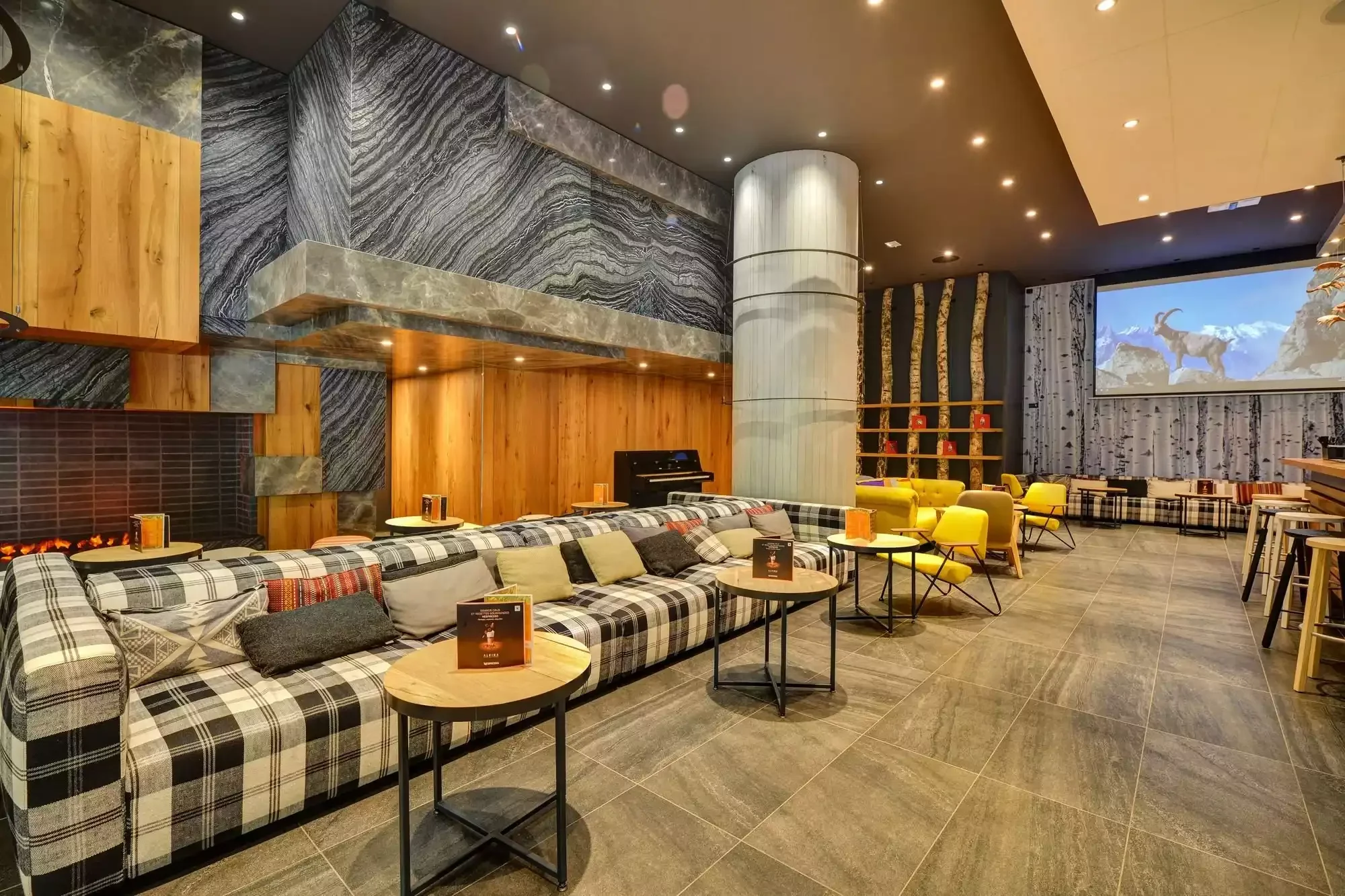 Salon moderne à l’Hôtel Alpina Chamonix, avec des canapés et fauteuils confortables aux couleurs vives, et un grand écran, créant un espace idéal pour la socialisation ou la détente.