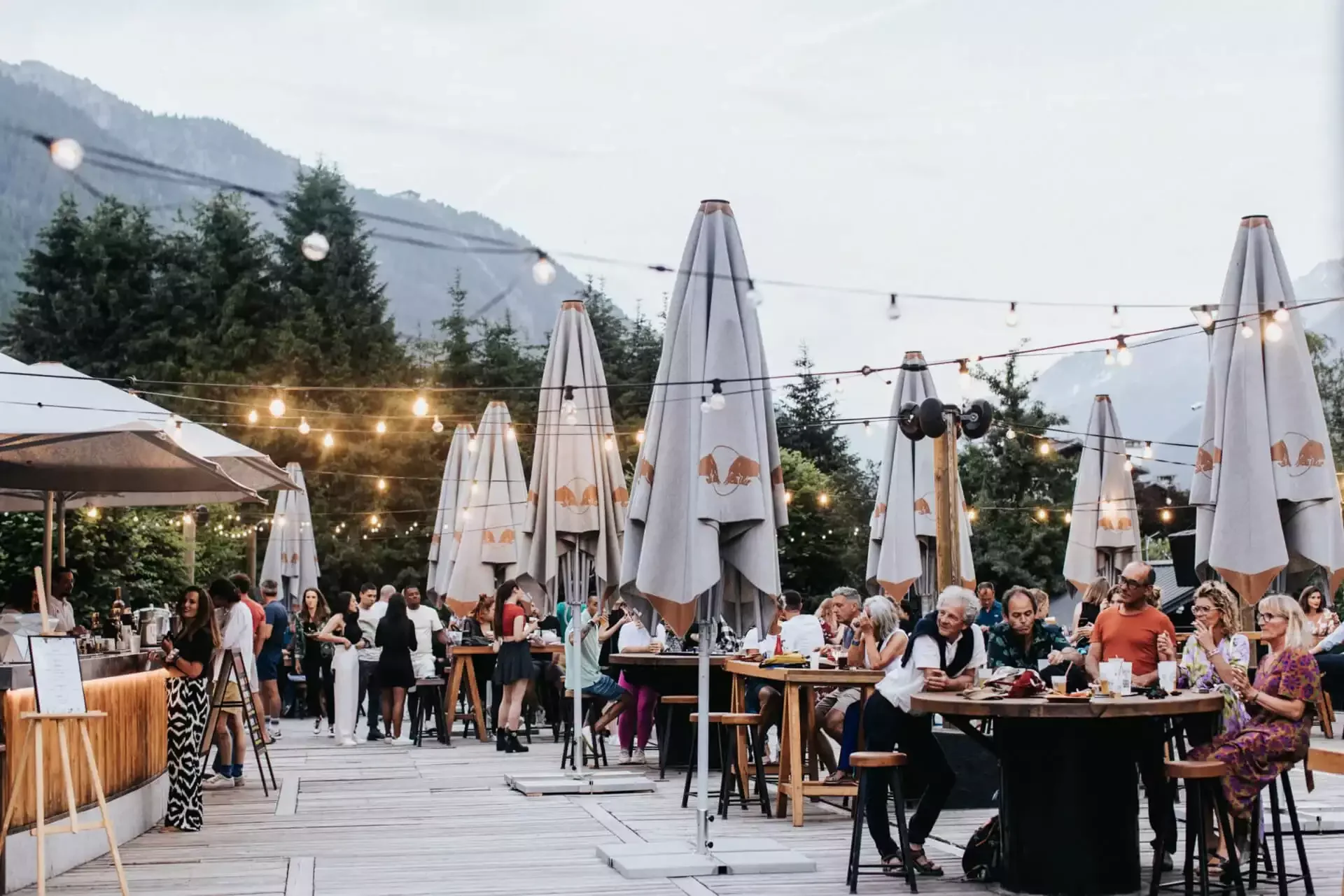 Événement social en plein air dans les jardins de l’Hôtel La Folie Douce 4*, avec des tables dînatoires sous des guirlandes lumineuses et des parasols, où les invités profitent d’une ambiance festive.