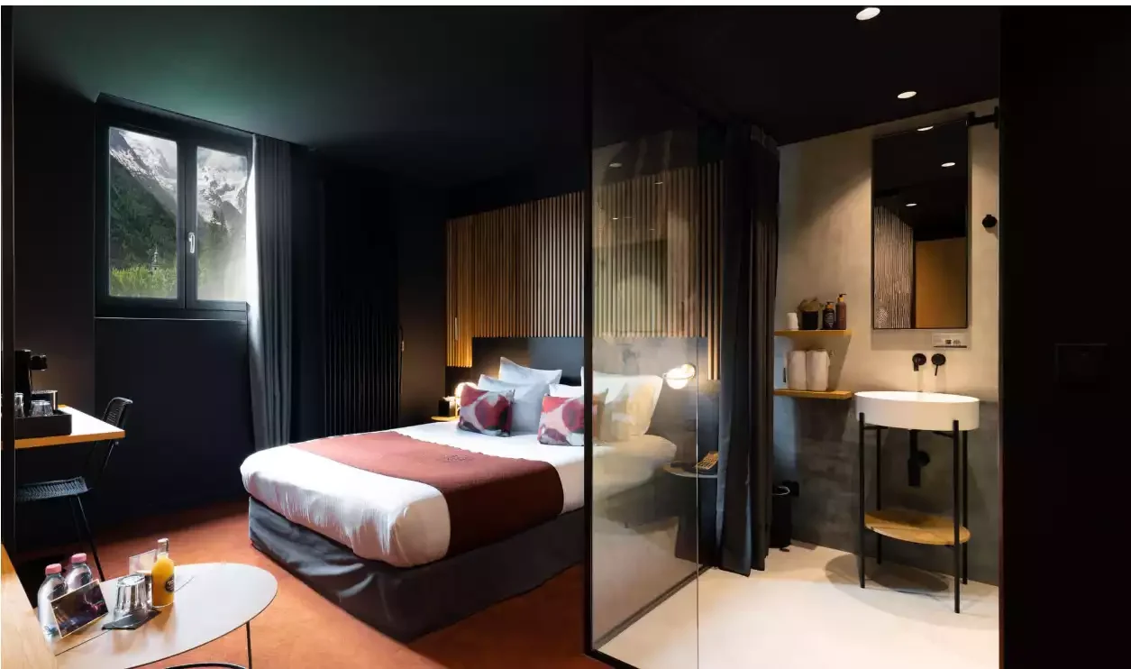 Chambre design moderne à l’Hôtel La Folie Douce 4*, aux murs sombres, avec un grand lit et une salle de bain intégrée avec lavabo, offrant un style contemporain et fonctionnel.