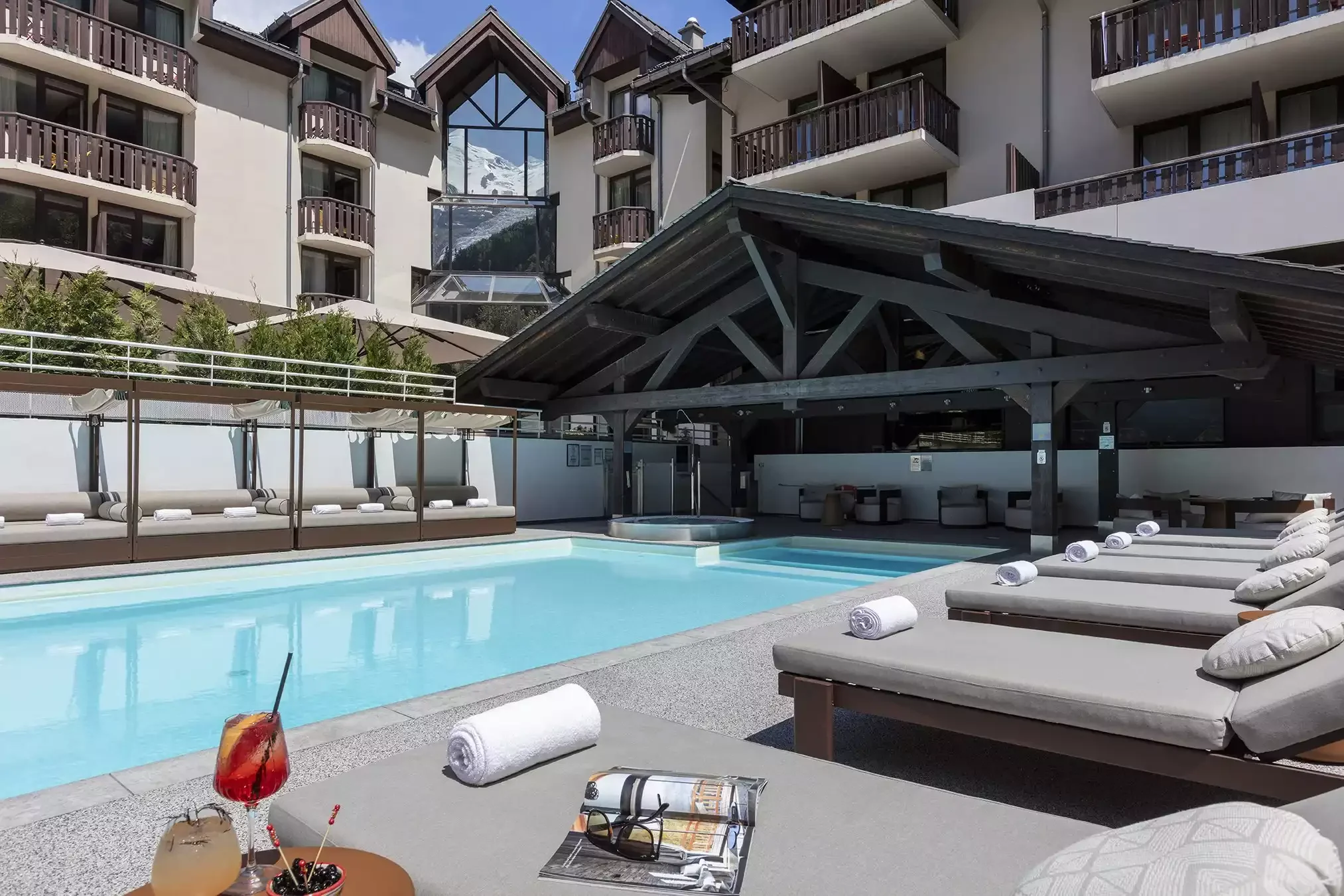 Piscine extérieure chauffée à l’Hôtel Les Aiglons de Chamonix, entourée de transats et avec un bar de piscine couvert. C’est un espace idéal pour se détendre.