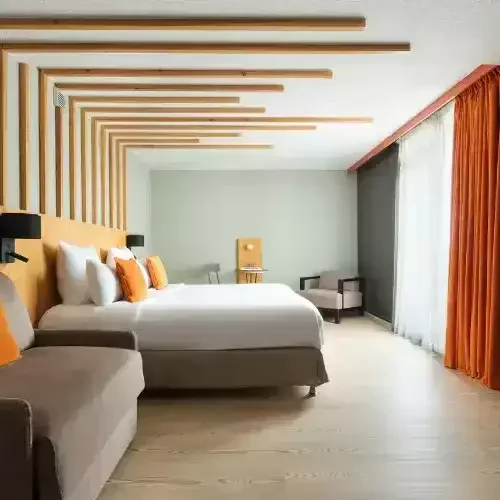 Chambre lumineuse à l’Hôtel Les Aiglons de Chamonix, avec un grand lit, une décoration moderne aux tons orangés et une tête de lit en bois, offrant une ambiance cosy.