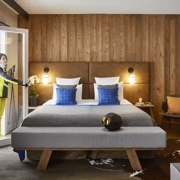 Chambre à l’Hôtel Ecrin Blanc avec murs en bois, un grand lit avec draps gris et oreillers bleus, créant une ambiance moderne et accueillante.