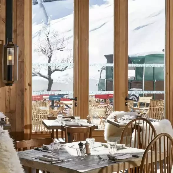 Espace restaurant ou lounge à l’Hôtel Ecrin Blanc, avec de grandes baies vitrées offrant des vues enneigées et un mobilier en bois aux touches modernes.