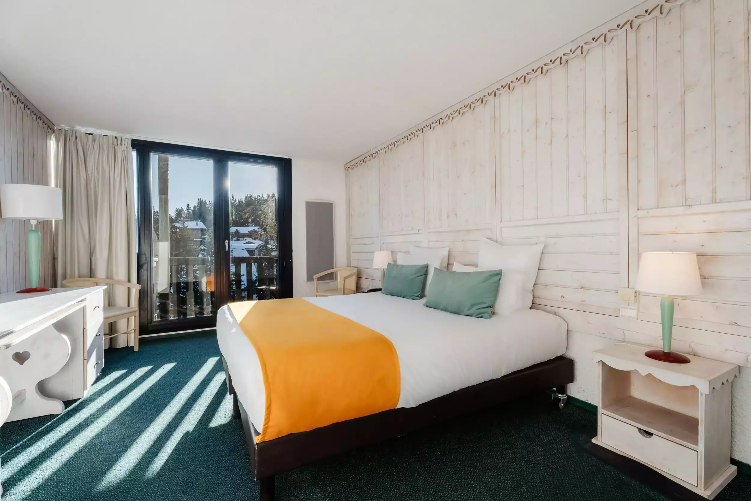 Chambre lumineuse à l’hôtel Lake Courchevel, avec un grand lit et un design moderne qui combine des éléments en bois. Un balcon avec vue sur les montagnes offre un espace pour se détendre.