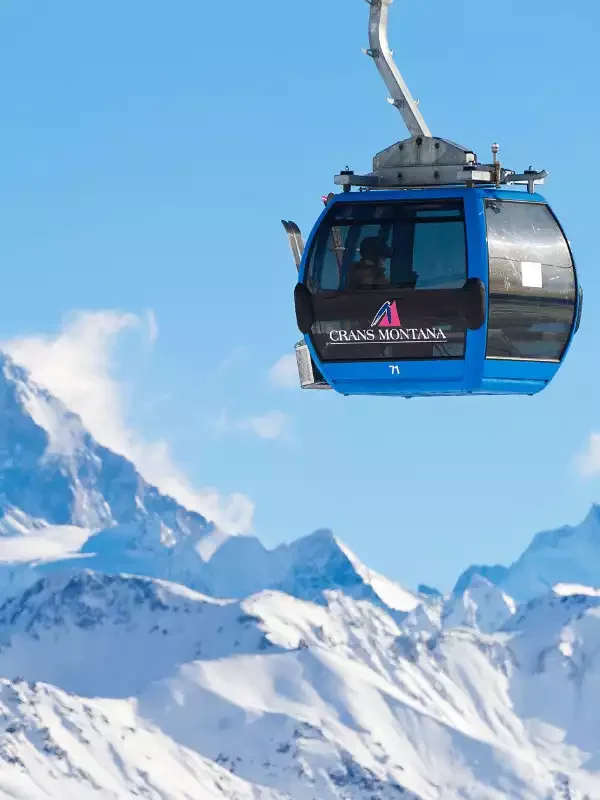 Une gondole bleue de la station de ski de Crans-Montana au séminaire d’Aylo Montagne,  sur les sommets enneigés et les montagnes, sous un ciel bleu éclatant.