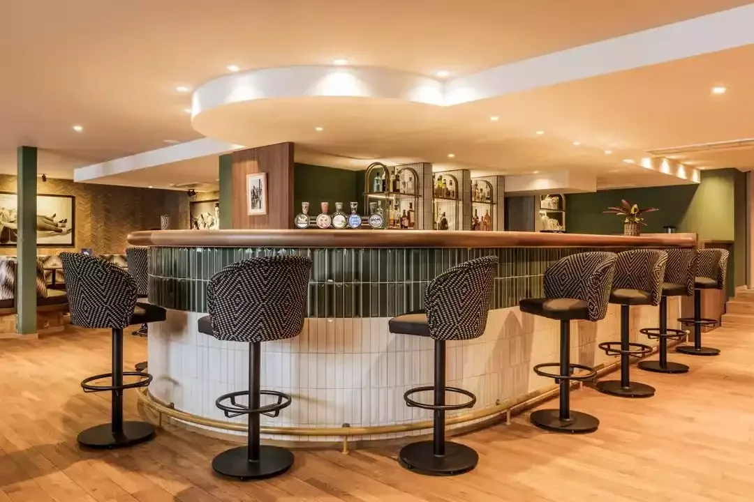 Bar de l’hôtel à Faern resorts Crans-Montana avec un comptoir circulaire et des tabourets modernes. L’espace, avec son éclairage chaleureux, est parfait pour socialiser.