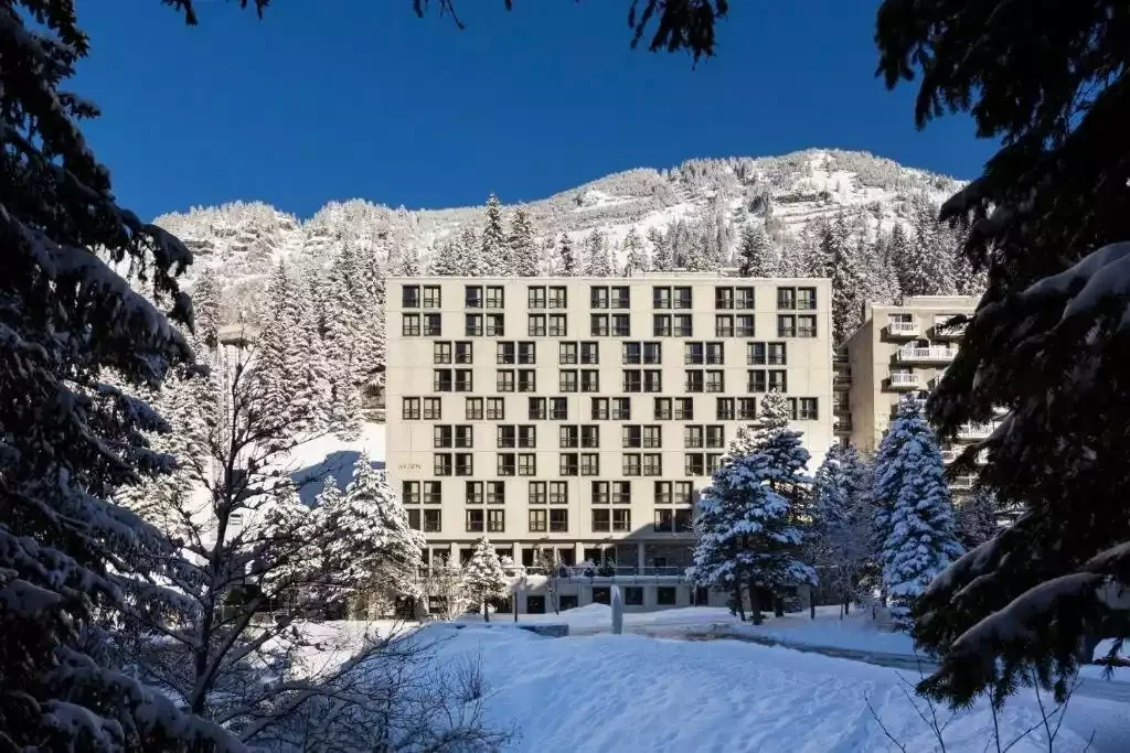 Vue extérieure de l’hôtel Rocky Pop à la gare de Flaine, un bâtiment moderne au design cubique entouré de neige et d’arbres alpins. Le cadre est idéal pour un séminaire d’Aylo Montagne.
