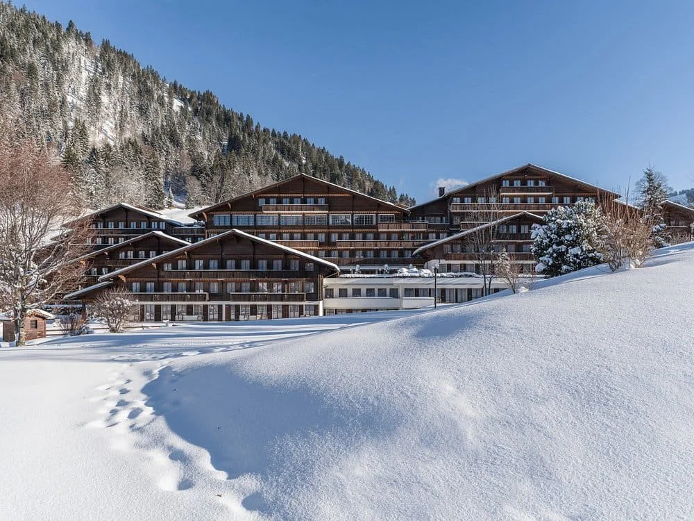 Vue extérieure de l’hôtel HUUS Gstaad en hiver, chalets alpins entourés de neige dans les montagnes suisses – Aylo Montagne.