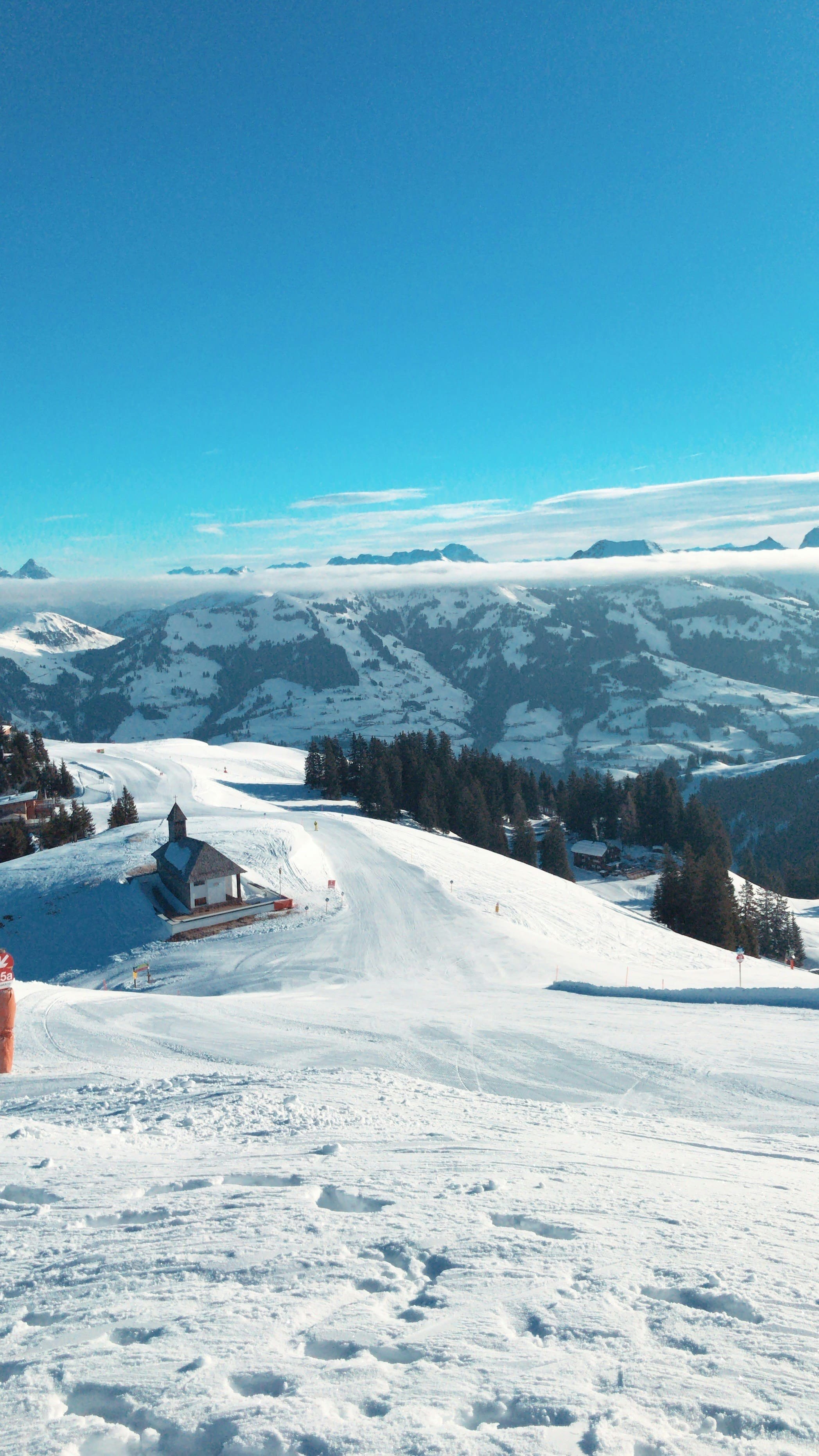 Panorama du domaine skiable de Kitzbühel, avec une piste enneigée, une petite chapelle d’altitude et les sommets du Tyrol – Séminaire à Kitzbühel – Aylo Montagne.