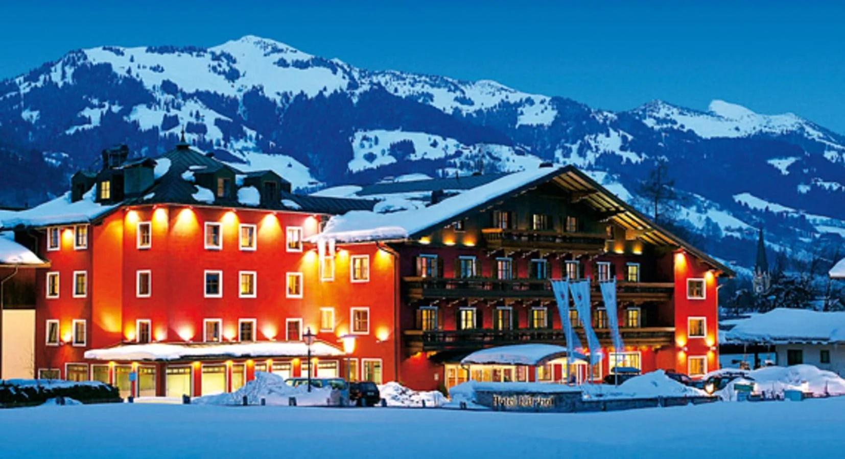 Façade illuminée du Kitzhof Mountain Design Resort 4★ à Kitzbühel, entourée de neige avec vue sur les montagnes du Tyrol – Séminaire d’entreprise à Kitzbühel – Aylo Montagne.