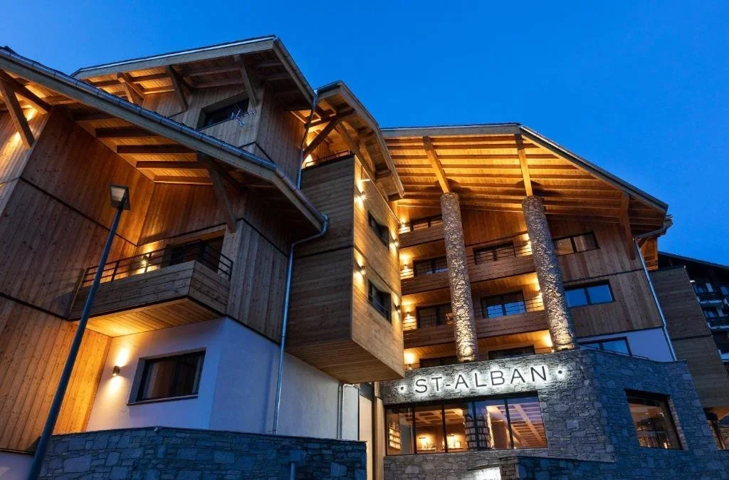 Vue nocturne de la façade de l’Hôtel St. Alban à La Clusaz. L’hôtel de style chalet moderne est éclairé, montrant son architecture en bois et pierre, idéal pour un séjour de luxe.
