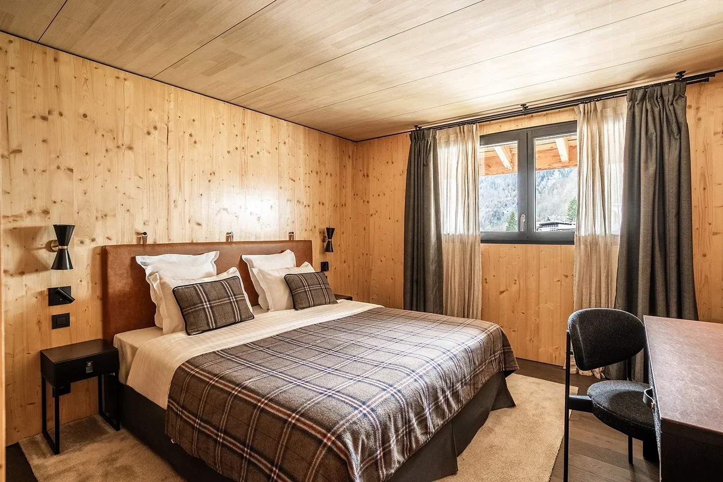 Chambre de l’hôtel St. Alban avec un design de style chalet, des murs en bois et un grand lit avec une couette à carreaux, offrant une atmosphère chaleureuse et rustique pour le repos.