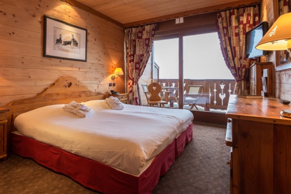 Chambre de style chalet à l’Hôtel La Carlina avec des murs en bois rustique, un grand lit et un balcon avec vue sur la montagne.