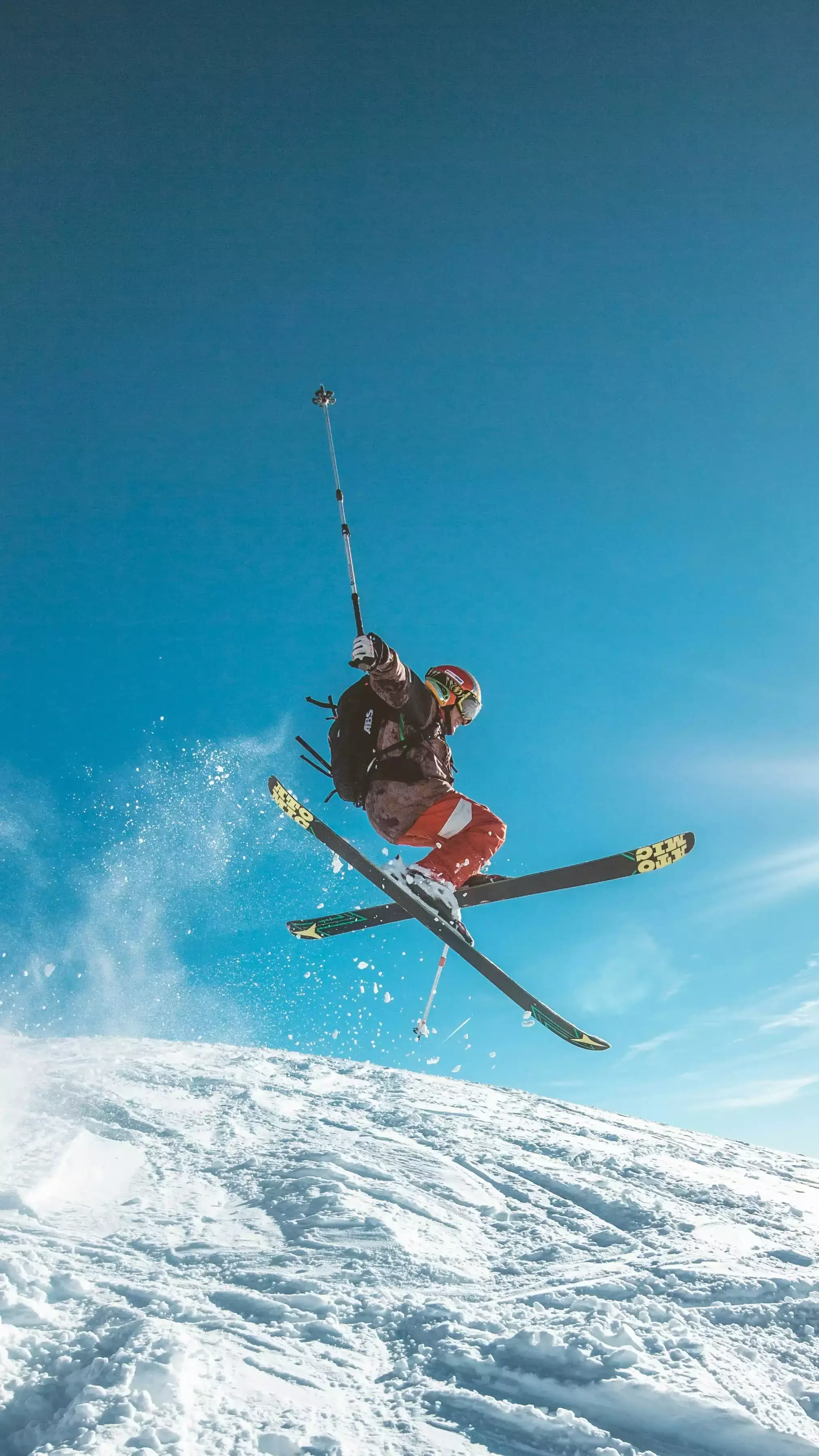 Un skieur de cross-country saute dans les airs sur une crête de montagne, portant un équipement de caméra sur un bâton.