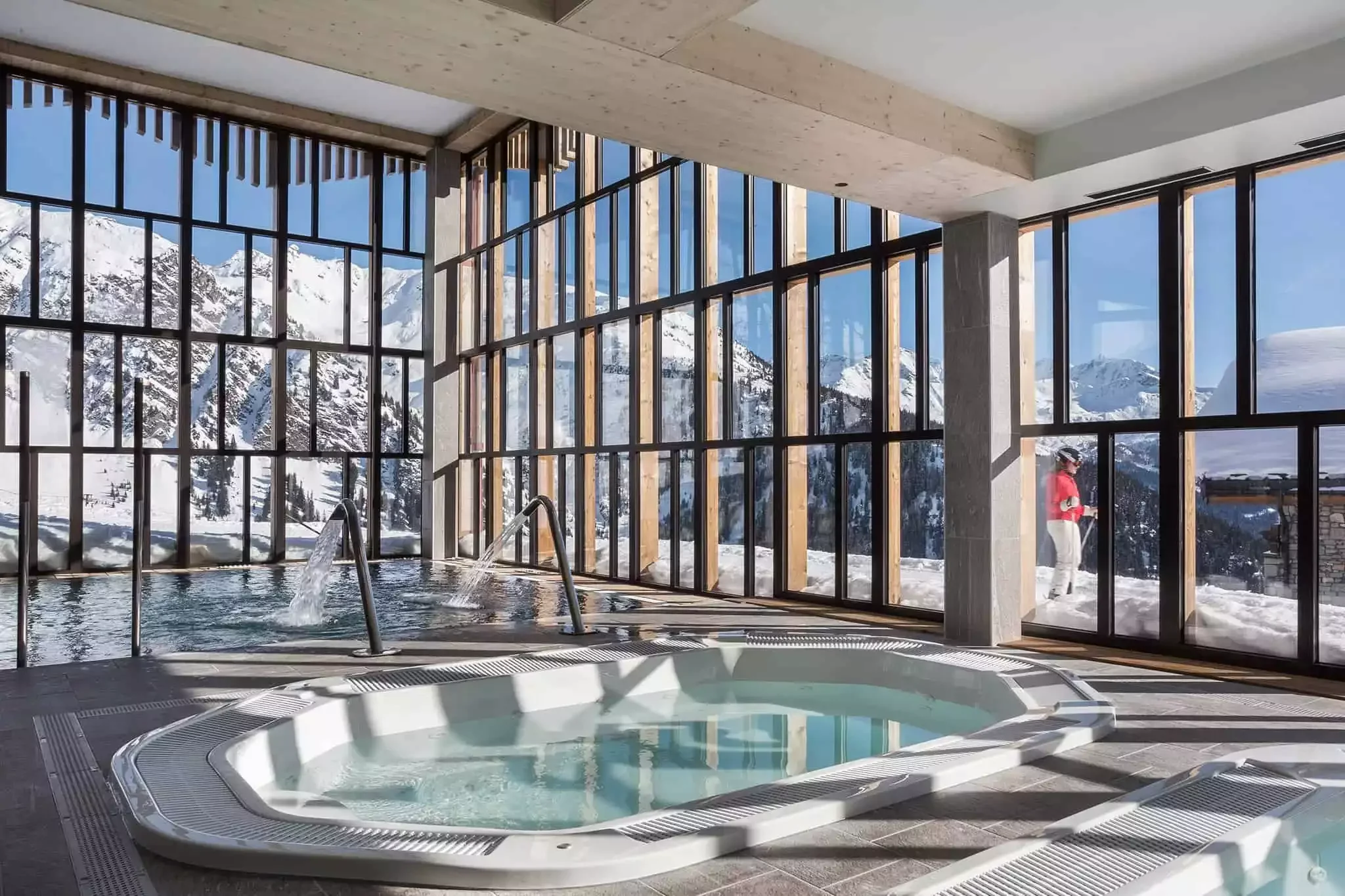 Piscine et jacuzzi intérieur à l’Hôtel Alparena, avec de grandes baies vitrées offrant une vue imprenable sur un paysage enneigé, créant un espace de détente et de bien-être.