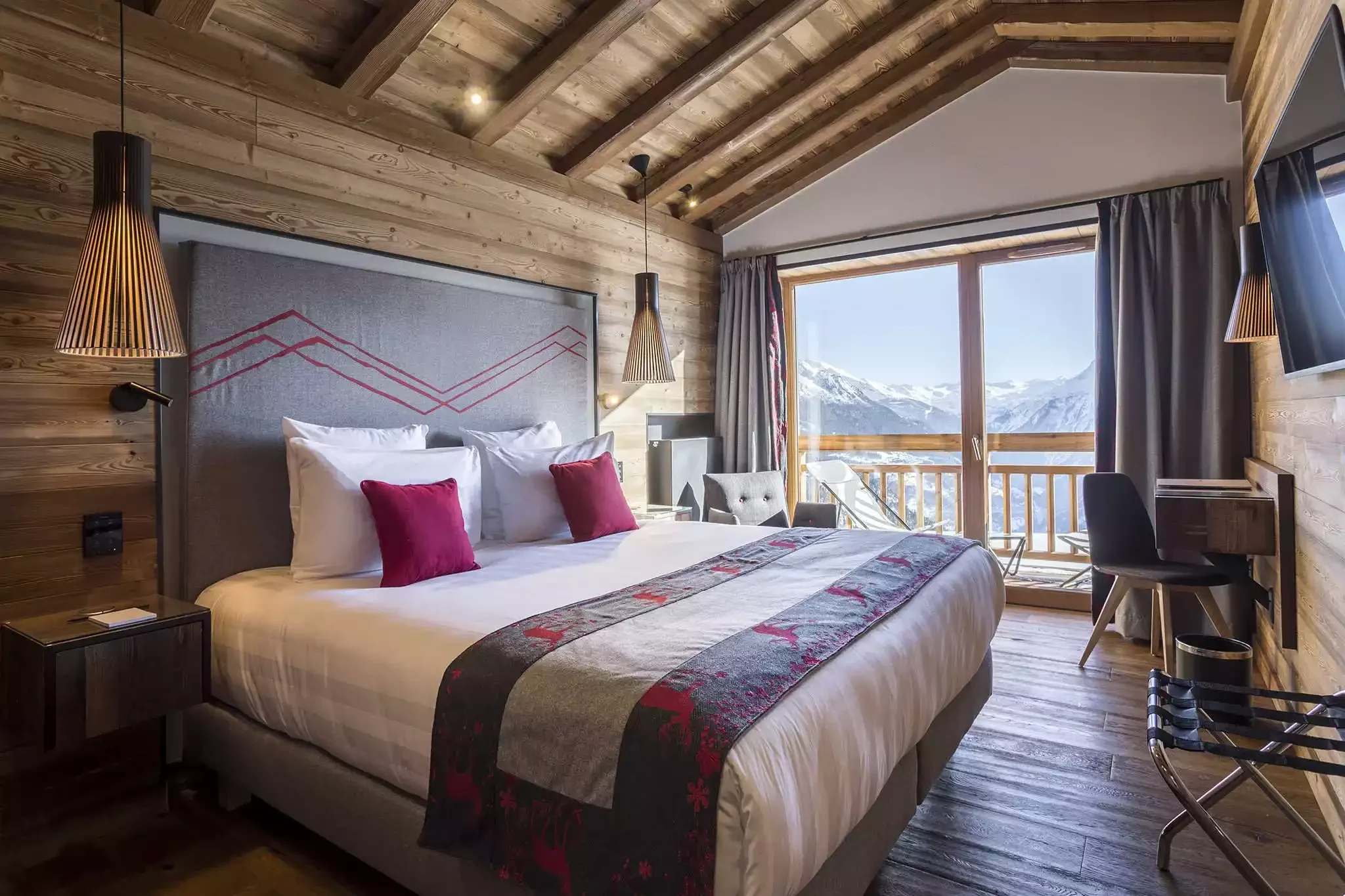 Chambre d’hôtel à l’Hôtel Alparena avec un style alpin moderne, plafond avec poutres apparentes, un grand lit et une grande fenêtre qui s’ouvre sur la montagne.