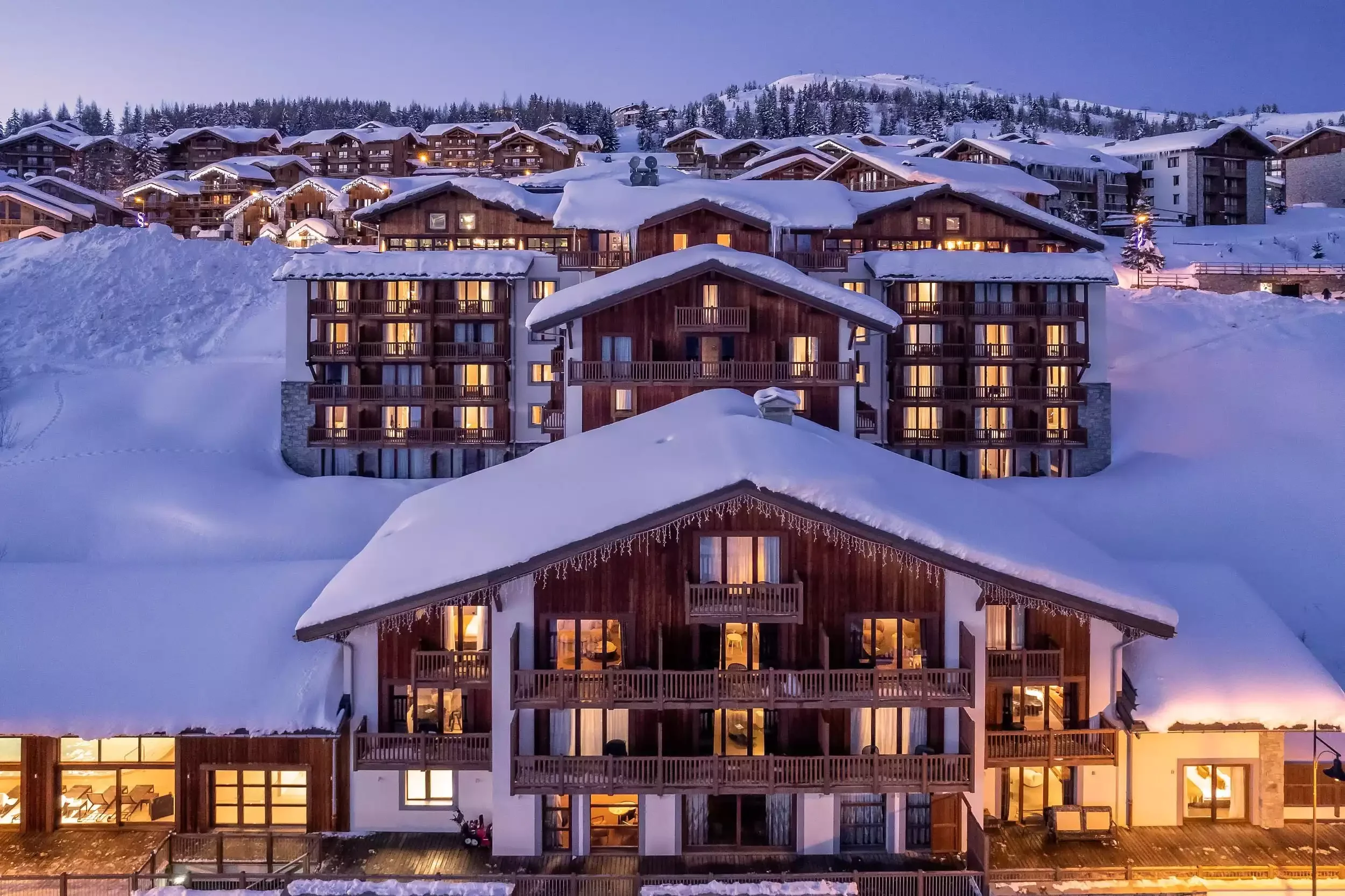 Vue nocturne de l’I.LY Hôtel à La Rosière. Les grands chalets en bois, recouverts de neige et éclairés par des lumières chaudes, créent une ambiance chaleureuse dans la montagne.