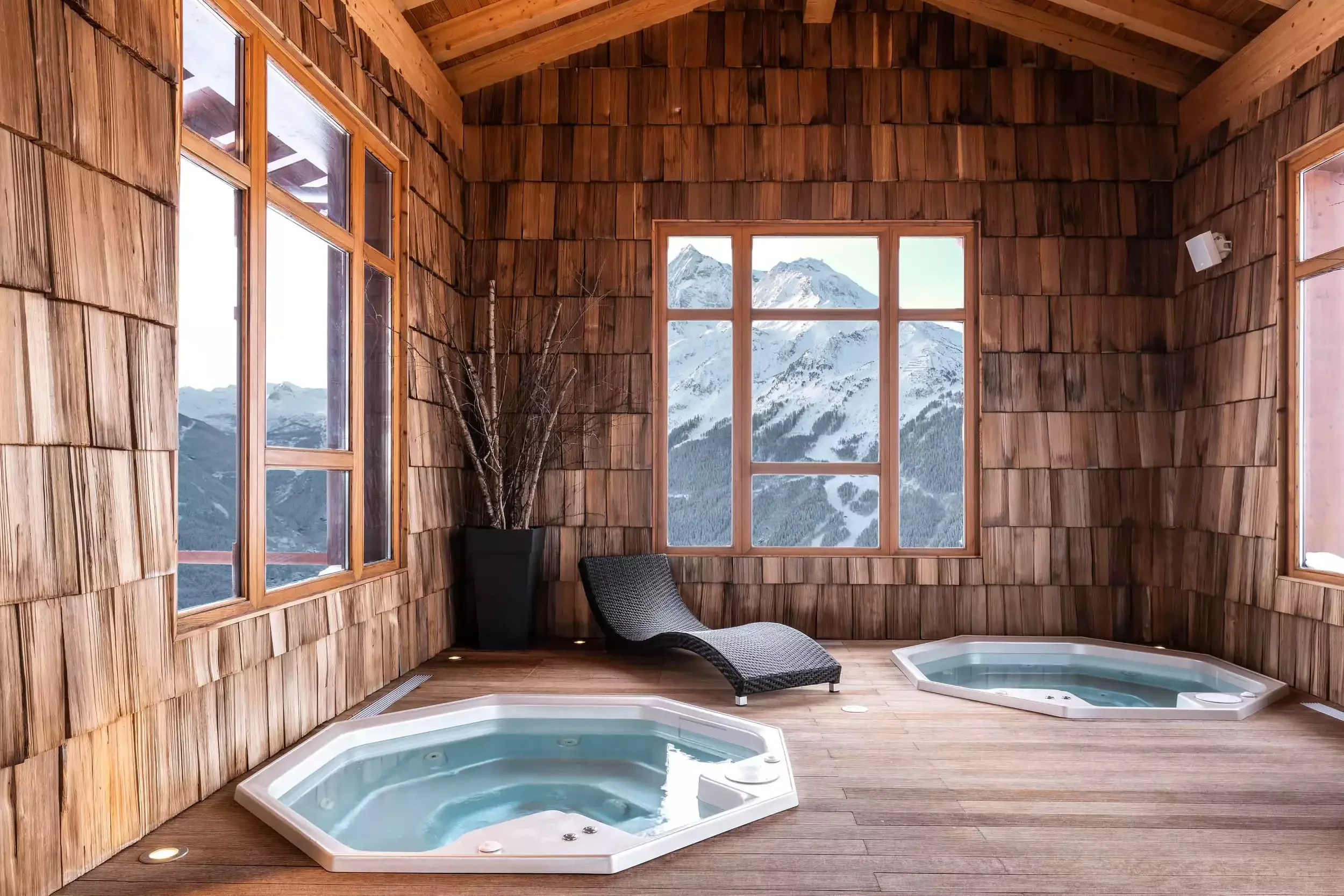 Espace spa de l’hôtel I.LY à La Rosière avec deux jacuzzis design et murs en bois rustique. Une grande baie vitrée offre une vue imprenable sur les montagnes enneigées.