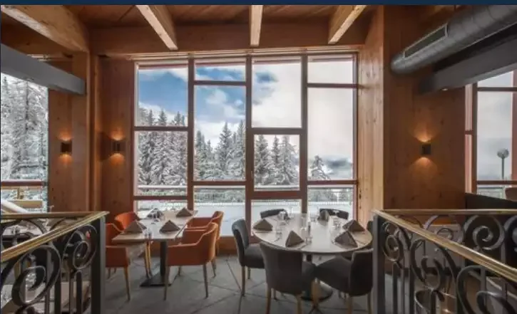 Restaurant de l’Altezza arc 1800 4* avec un buffet préparé pour le service. Le salon a un design moderne qui combine bois et couleurs vives, créant une atmosphère accueillante pour les invités.