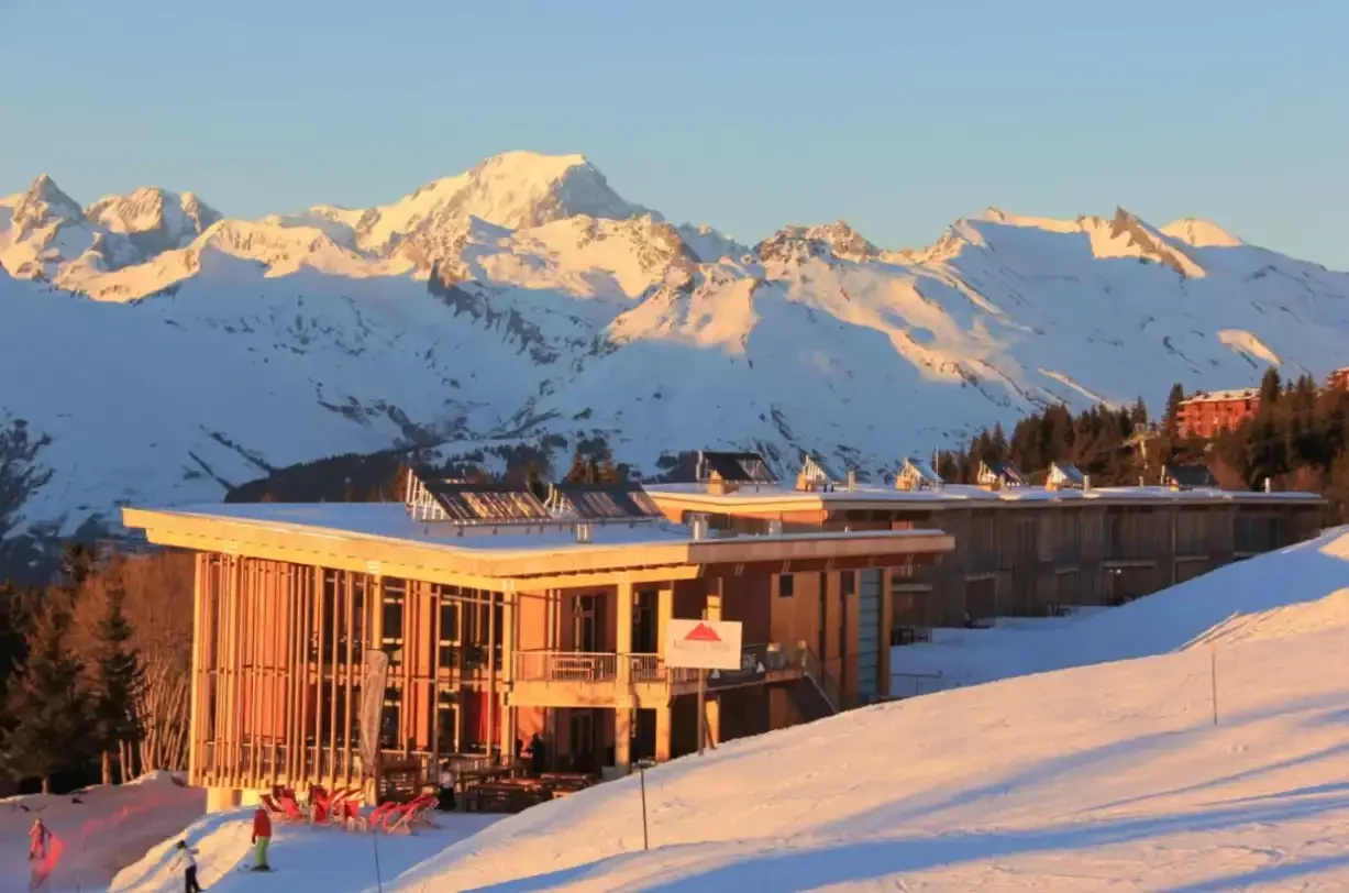 Vue sur l’hôtel Aiguille Grive Chalets 4* à Les Arcs al atarzers. L’hôtel, d’une architecture moderne et mature, est situé au pied des huttes, avec le soleil éclairant les majestueuses montagnes enneigées en bas.