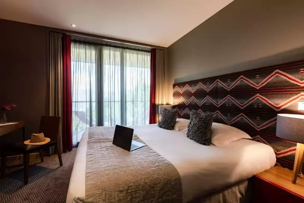 Chambre d’hôtel à l’Aiguille Grive avec un grand lit et une tête de lit avec un motif en zigzag. Un balcon avec vue sur la montagne est idéal pour travailler ou se détendre dans une ambiance moderne.