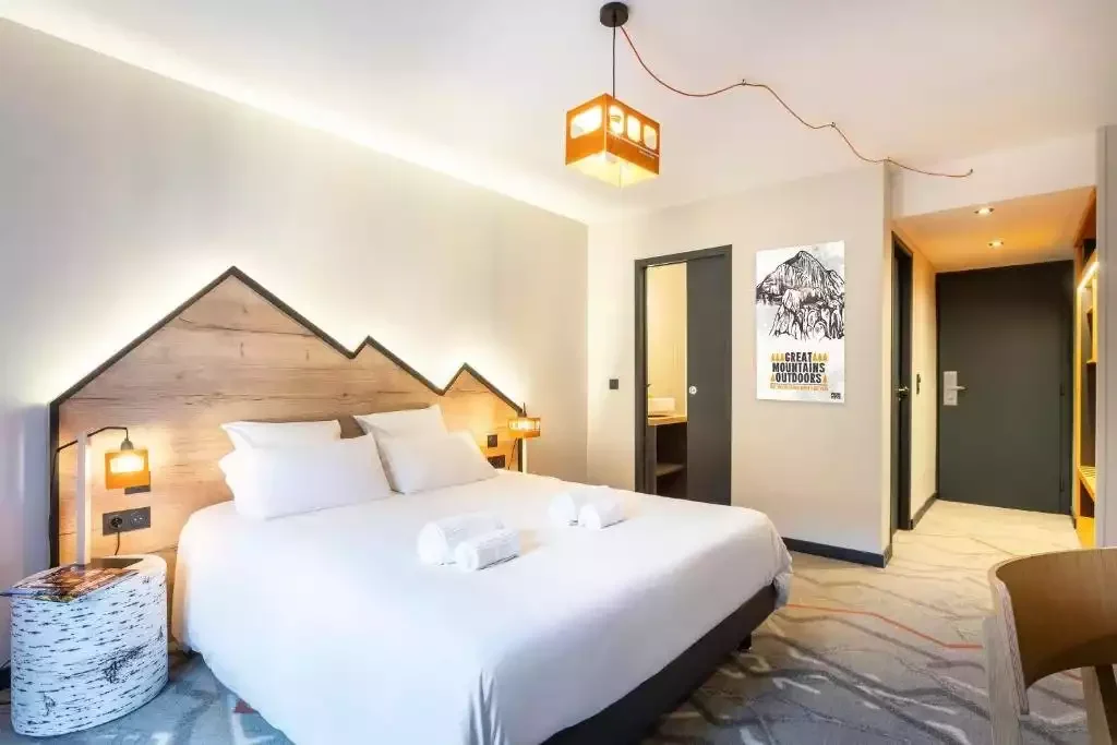 Chambre d’hôtel à la Base Camp Lodge, avec une tête de lit en forme de pic de montagne et un grand lit, créant une ambiance alpine moderne.