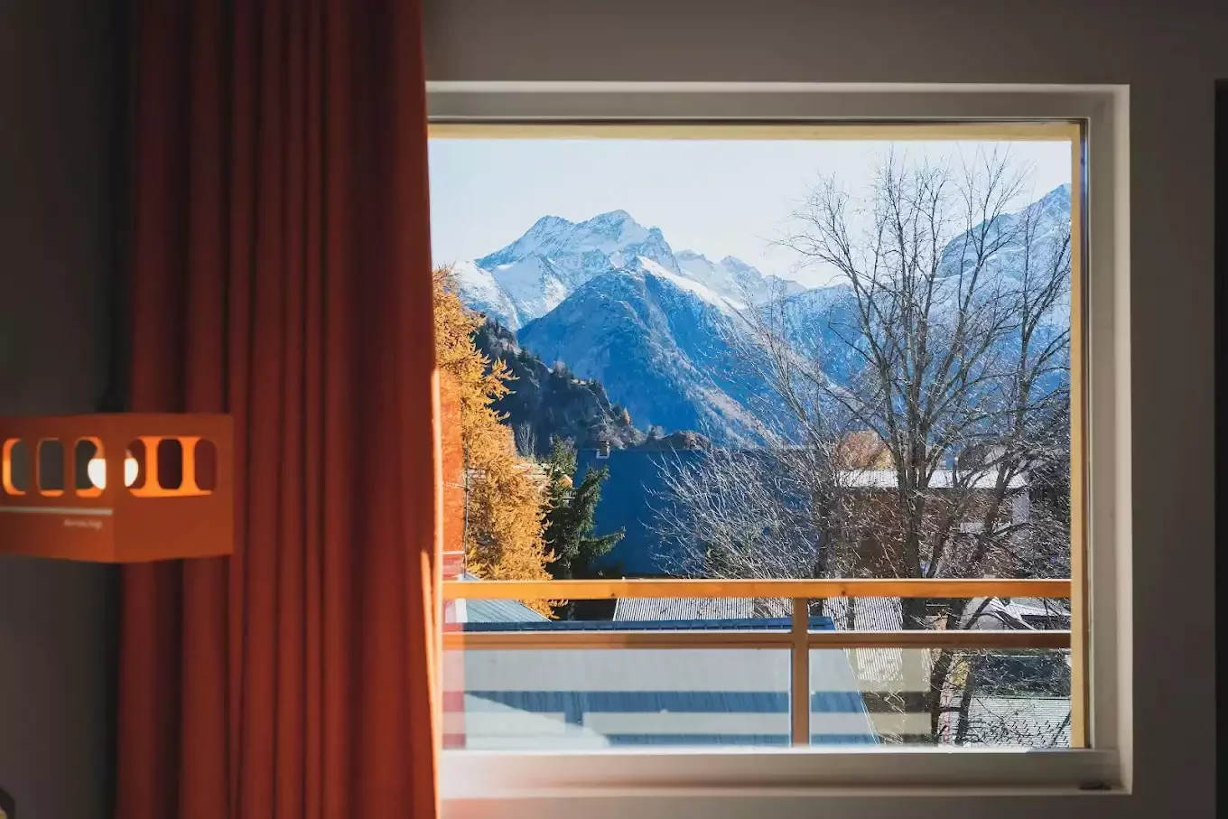 Vue d’une fenêtre de Base Camp Lodge sur un paysage de montagne en automne. Les montagnes alpines et le feuillage des arbres créent une vue à couper le souffle.