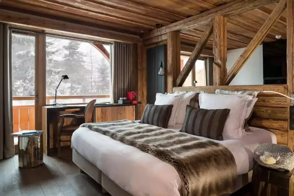 Chambre d’hôtel au Chalet Mounier avec un design rustique en bois, un grand lit et un balcon donnant sur un paysage enneigé, créant une atmosphère chaleureuse et traditionnelle.