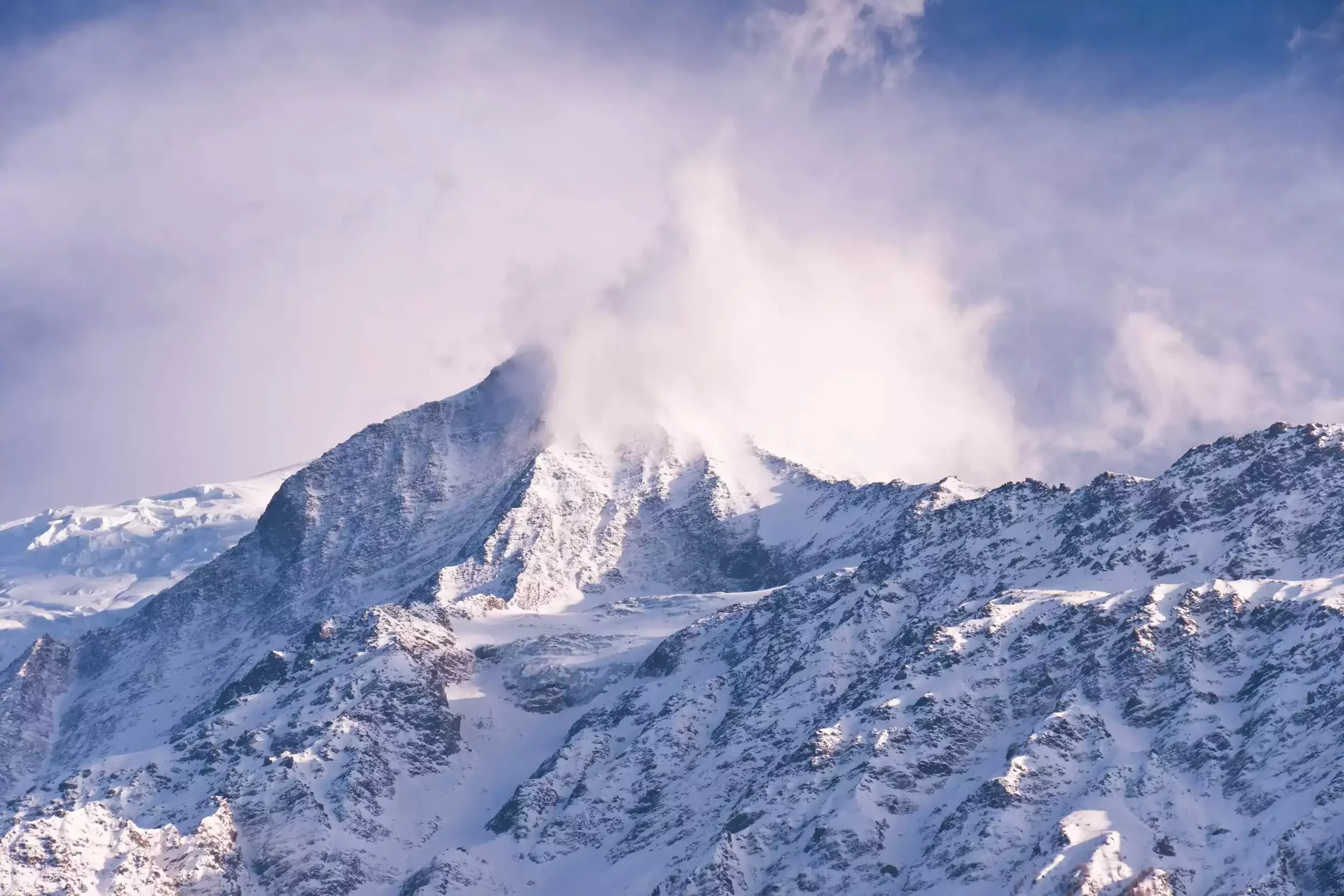 Un majestueux pic de montagne enneigé aux Houches, avec des nuages qui l’enveloppent. L’image montre le sommet de la montagne par une journée partiellement nuageuse.