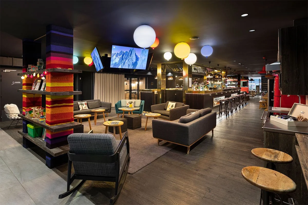 Grand hall d’hôtel dans le Rocky Pop Hotel avec un design coloré et moderne. Des canapés et des fauteuils de différentes couleurs créent un espace social et accueillant pour les invités.