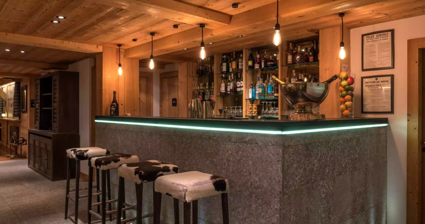 Bar d’hôtel de luxe à l’Hôtel Granges d’en Haut, avec un comptoir éclairé et un design moderne en bois. L’espace est idéal pour prendre un verre dans une ambiance sophistiquée.