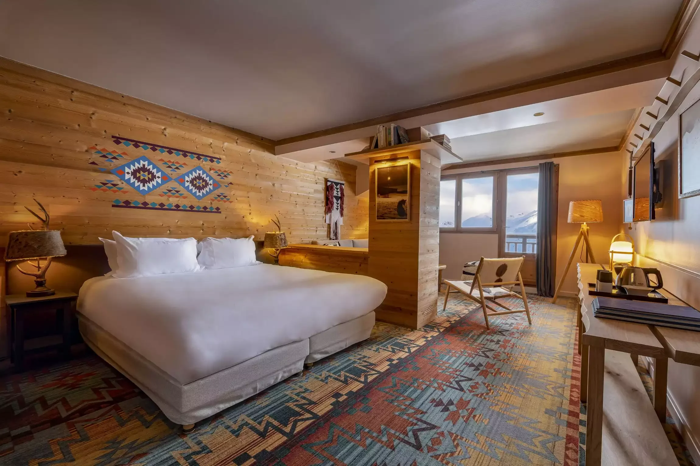 Chambre d’hôtel à l’Hôtel Kaya avec des murs en bois et un grand lit avec un tapis de motifs. C’est un espace de design alpin accueillant, avec vue sur la montagne.