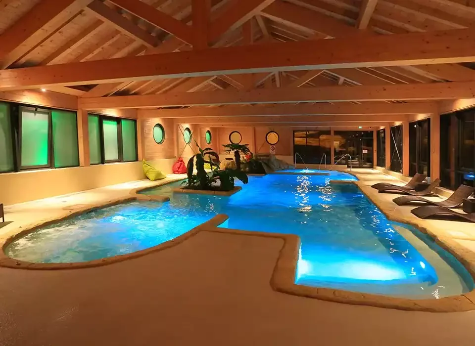 Piscine intérieure du spa au Chalet Hôtel et Spa Le Meuire. La piscine, avec un éclairage bleu et un jacuzzi, est idéal pour la détente et le repos après une journée de ski.