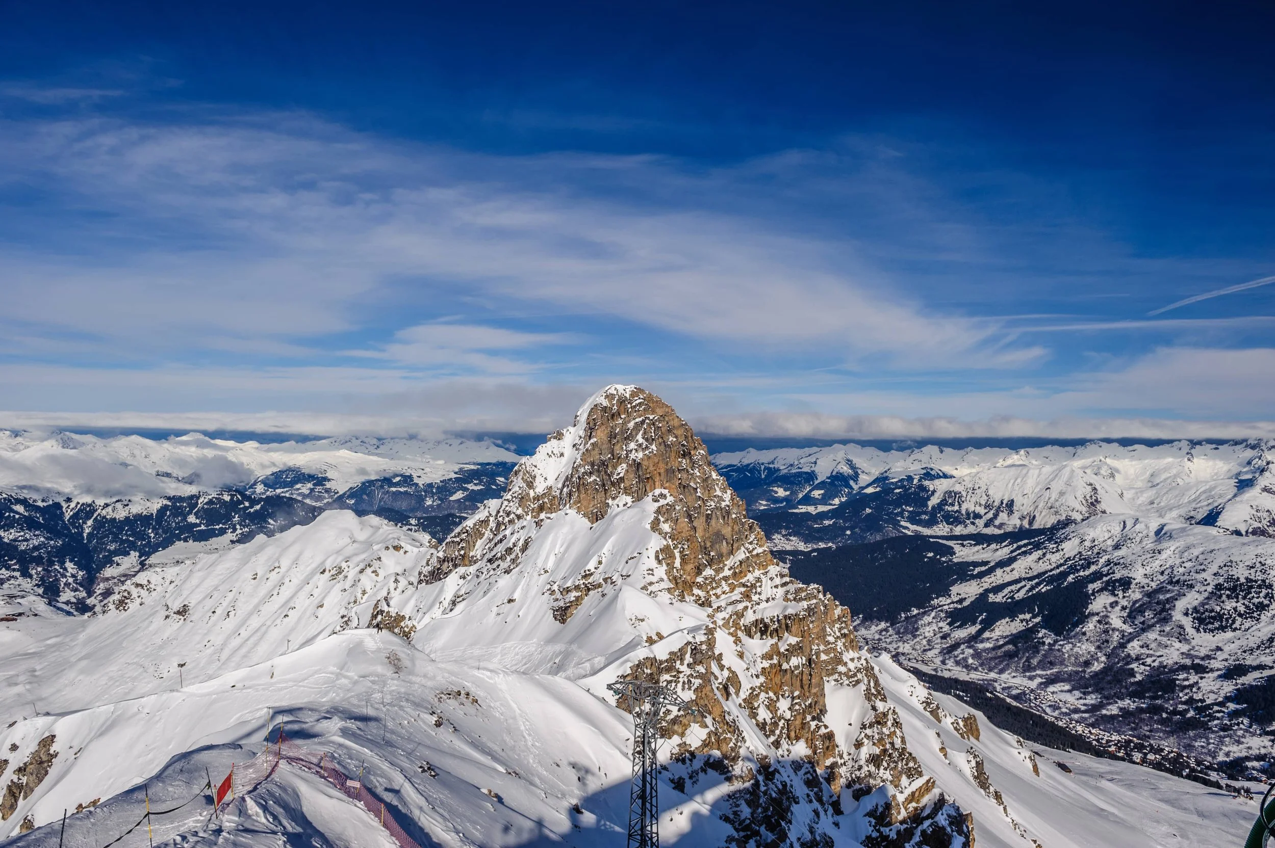 Vue panoramique sur le majestueux pic enneigé de l’Aiguille du Fruit à Méribel, avec un paysage de montagnes alpines couvertes de neige et un ciel bleu avec des nuages épars.