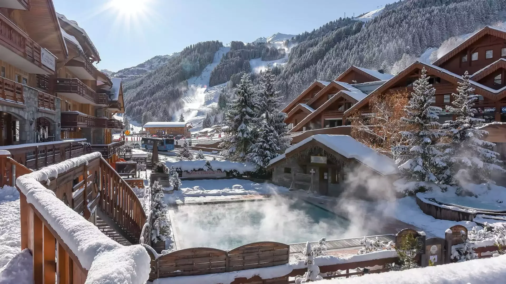 Jacuzzi extérieur à l’Hôtel L’Eternlou, avec de l’eau fumante qui contraste avec le paysage enneigé. En arrière-plan se trouvent des chalets en bois, créant une atmosphère de détente et de luxe dans la montagne.