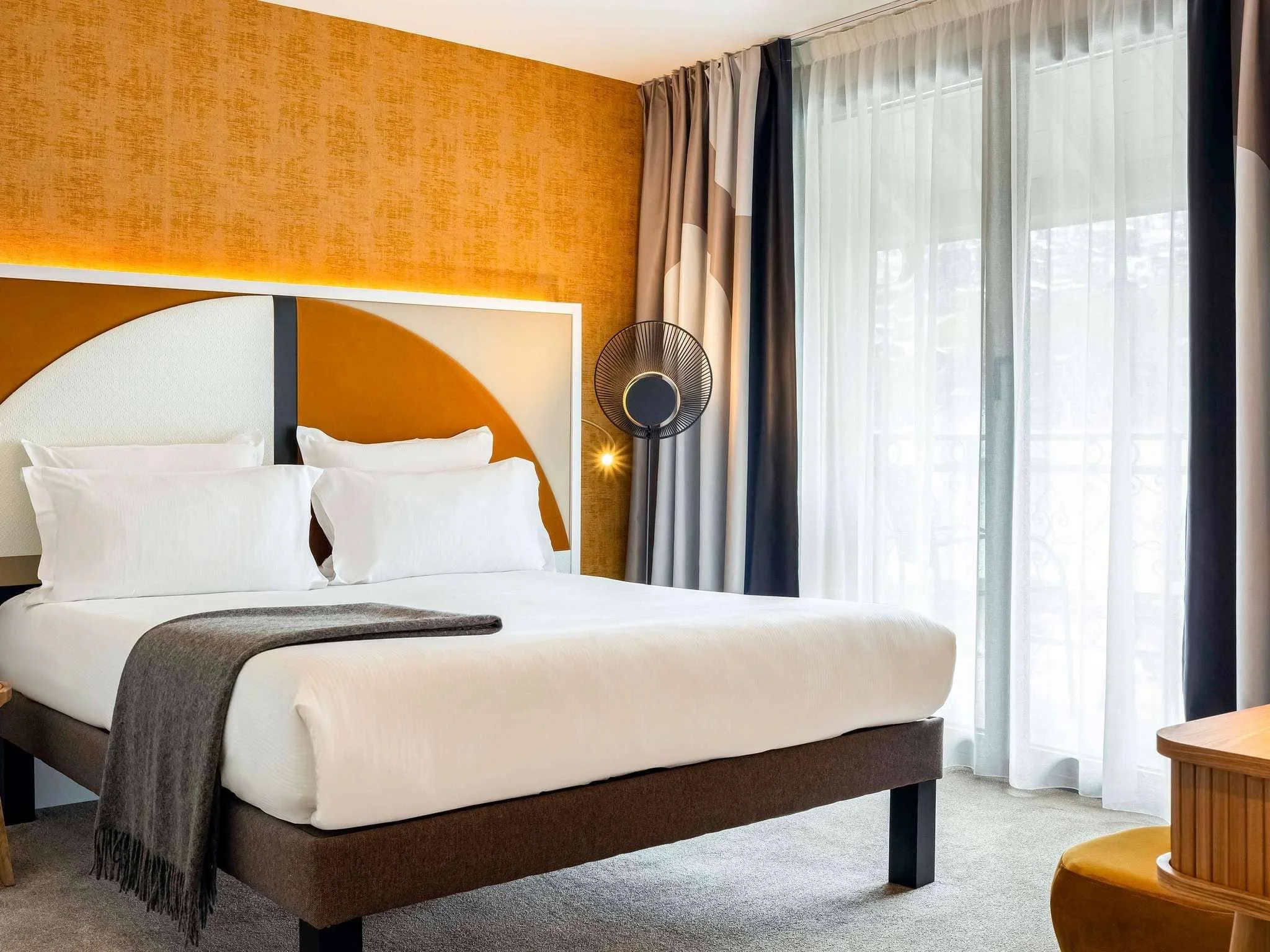 Chambre de luxe à l'Hôtel Saint Gervais avec une tête de lit design et des accents orange. L'espace moderne et lumineux est idéal pour le repos des participants d'un séminaire Aylo Montagne.