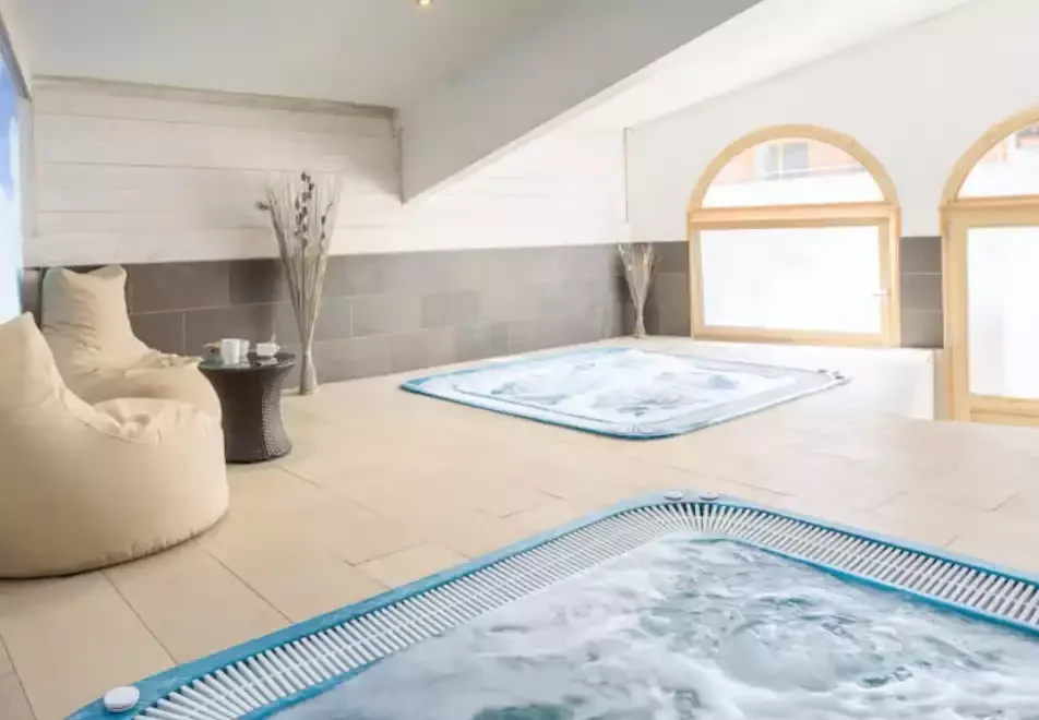 Espace spa du Club MMV Les Brévières 4* avec deux jacuzzis. L’espace, avec des murs en bois clair et de grandes fenêtres, est idéal pour se détendre après une journée dans la neige.