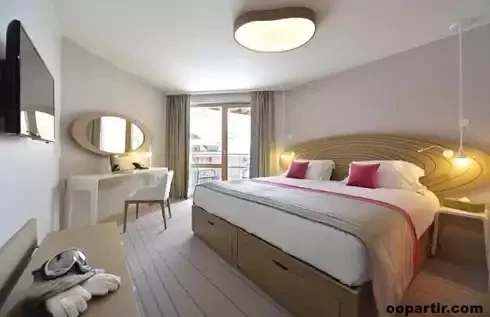Chambre d’hôtel au Club Med Val Thorens Sensations avec un design moderne, lit avec tête de lit en bois clair et une grande baie vitrée avec vue sur la montagne.